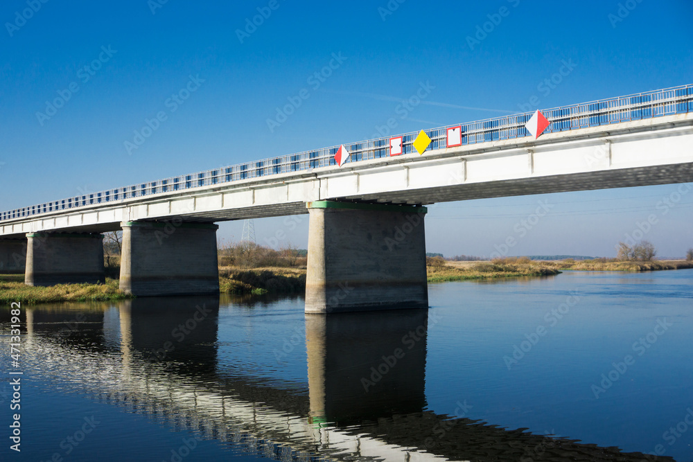 Road bridge with blue sky in the background. View from side. Straight road line with empty copy space. Old rusty road barriers texture. Bridge over river landscape.