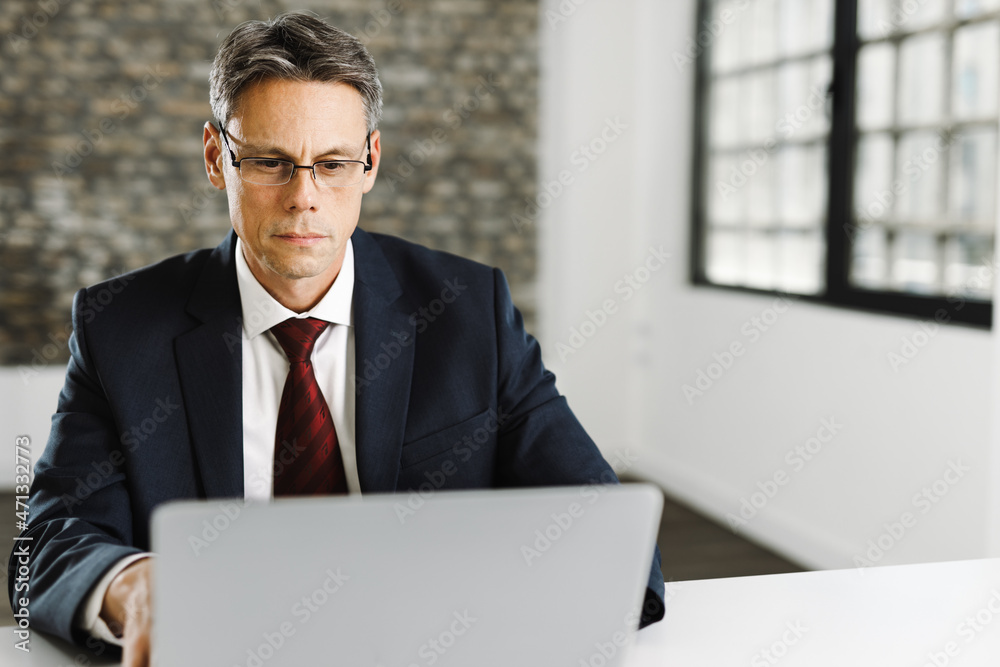 Mid adult businessman typing an e-mail on laptop in the office Mid adult businessman typing an e-mail on laptop in the office