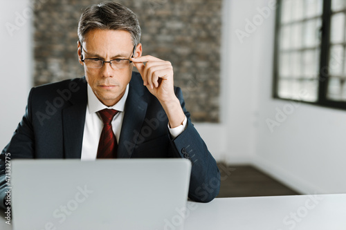 Mid adult businessman reading an e-mail on laptop in the office