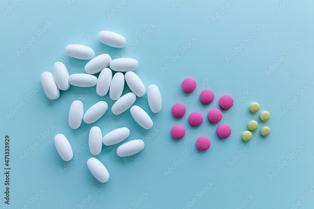 A bunch of white, pink and yellow pills on a light blue background.