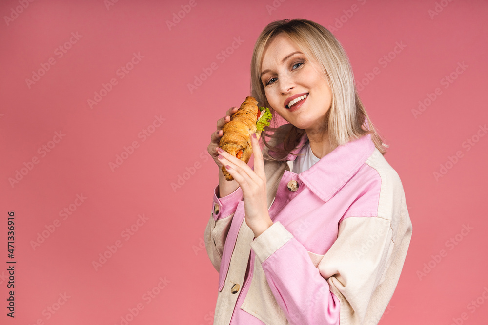Portrait of young beautiful hungry woman eating croissant sandwich. Isolated portrait of woman with fast food over pink background. Diet concept. Portrait of young beautiful hungry woman eating croissant sandwich. Isolated portrait of woman with fast food over pink background. Diet concept.
