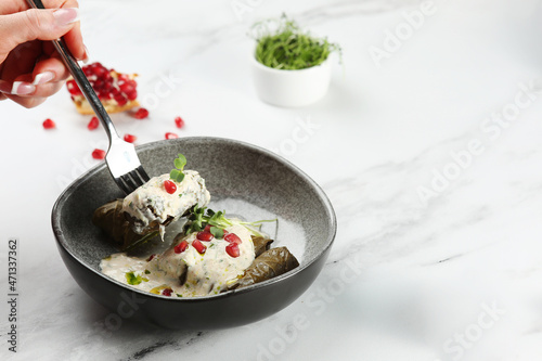 Delicious stuffed grape leaves traditional doom Mediterranean cuisine Dolma with pomegranate fruit on background. Womans hand hold fork witj dolma on light marble background.