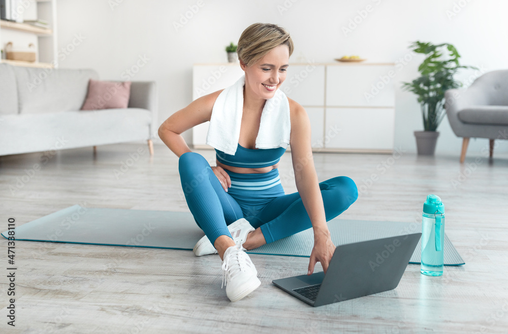 Smiling woman sitting on yoga mat using laptop