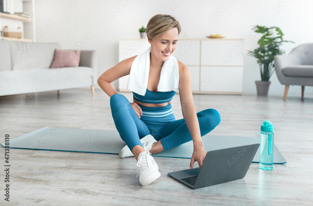 Smiling woman sitting on yoga mat using laptop Smiling woman sitting on yoga mat using laptop