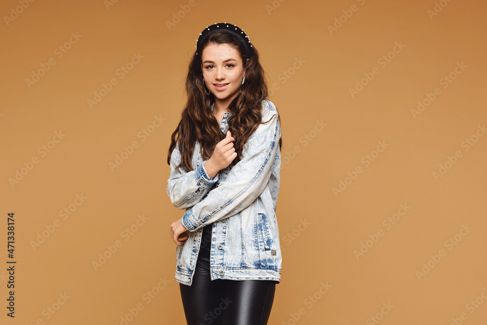 Adorable female model with natural makeup and wavy hairstyle wearing a denim jacket on the beige background with copy space Adorable female model with natural makeup and wavy hairstyle wearing a denim jacket on the beige background with copy space
