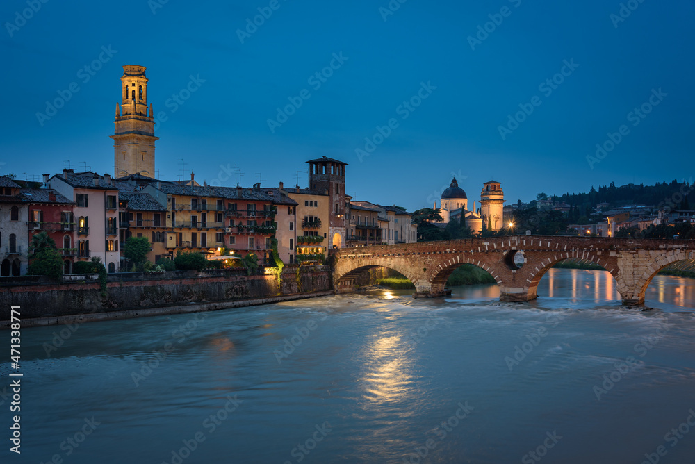 City landscape with the old town buildings along the bank of the Adige river and the famous Stone Bridge (Ponte di Piettra) at night, Verona, Veneto Region, Italy
