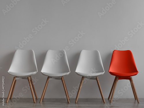 Three vacant white chairs and one red on gray wall background in office or room photo