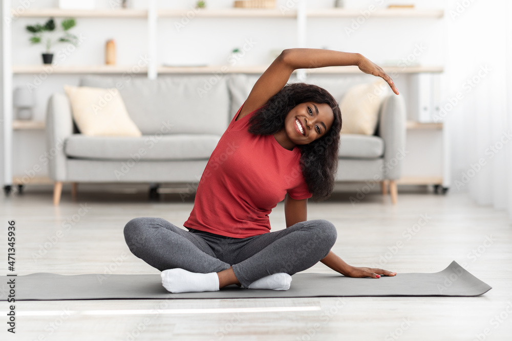 Fototapeta premium Cheerful african american woman stretching her body at home