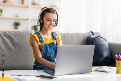 Girl sitting on couch using laptop, wearing headset photo