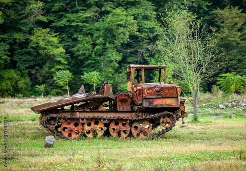 Old rusty all-terrain vehicle on tracks in an open field near the forest