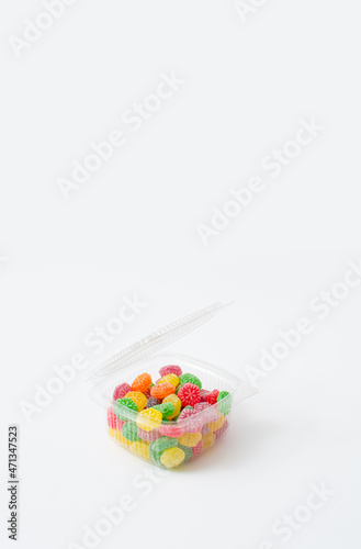 Delicious sweets in the plastic box on a white background. Sugar candies in red  green  yellow  orange and purple. A modern concept of sweets.