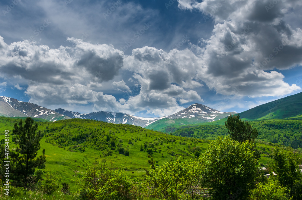 Obraz premium Spring landscape with snowy mountains and dramatic clouds 