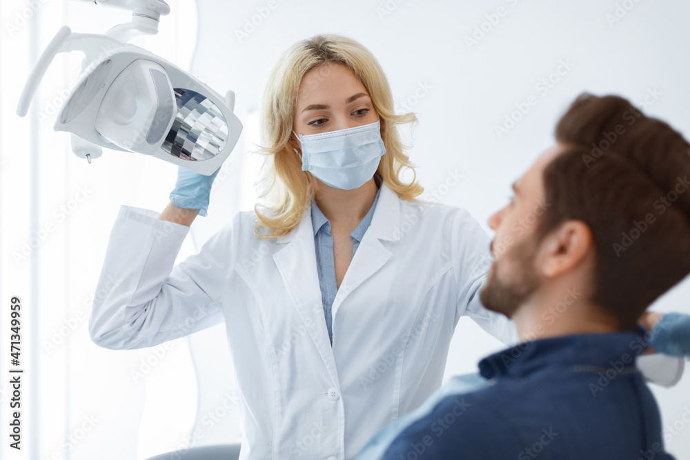 Female dentist in face mask greeting male patient