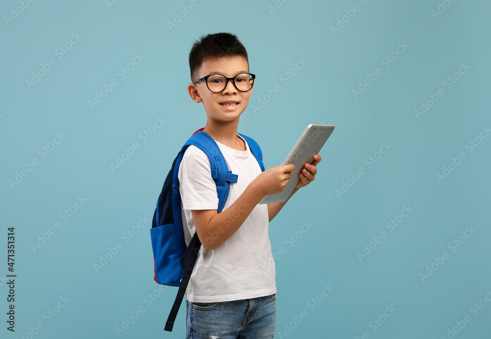 Distance Learning. Smiling Asian Schoolboy Wearing Eyeglasses And Backpack Holding Digital Tablet Distance Learning. Smiling Asian Schoolboy Wearing Eyeglasses And Backpack Holding Digital Tablet