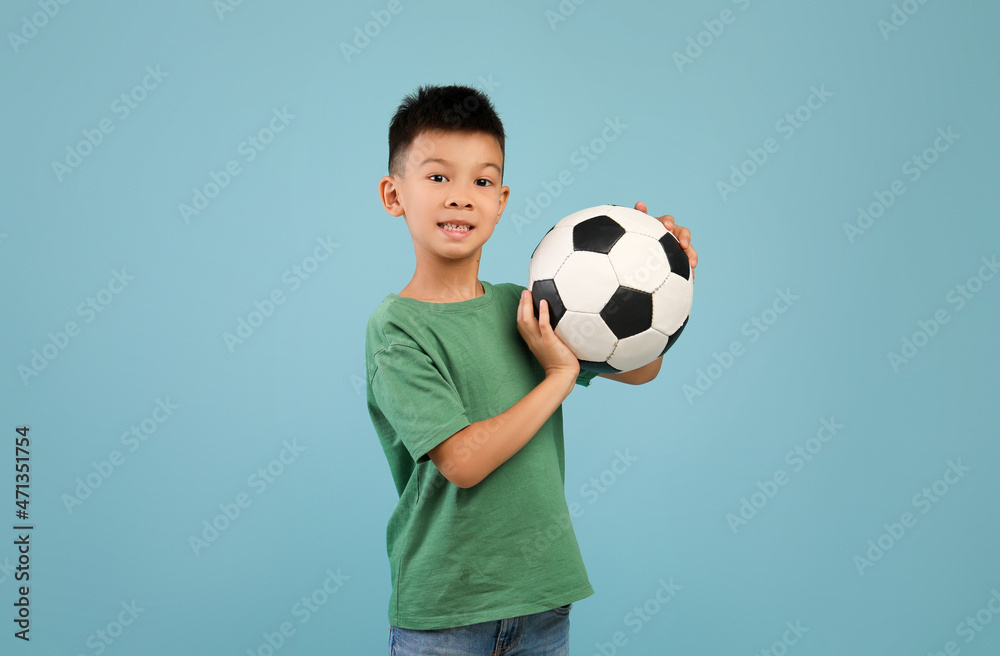 Little Sportsman. Excited Asian Boy Posing With Football Ball In Hands Over Blue Background Little Sportsman. Excited Asian Boy Posing With Football Ball In Hands Over Blue Background