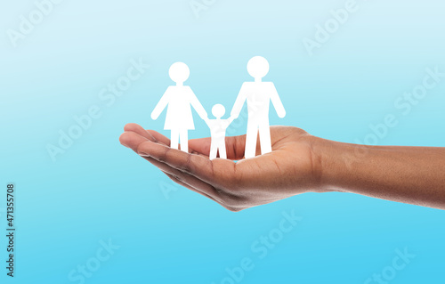 Male mixed race hand holds silhouette of people, mother, father and child on blue background