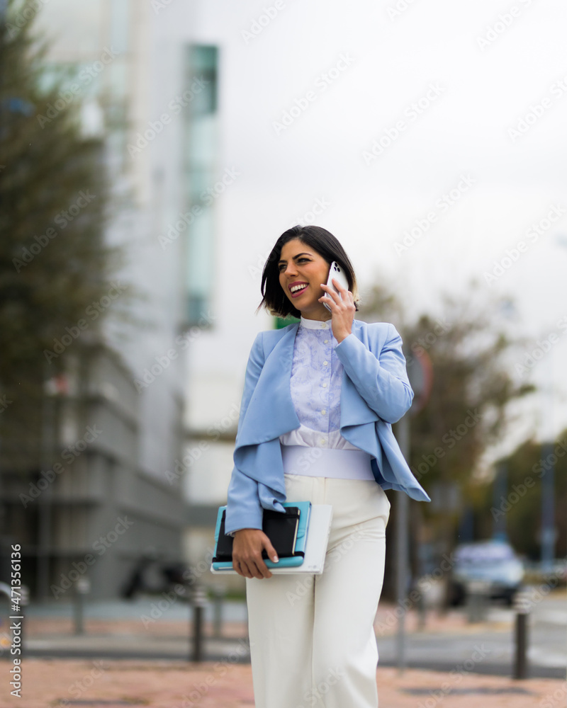 Successful woman talking on her smartphone while walking down the street smiling