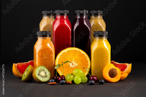 Flat-lay of colorful smoothies in bottles with fresh tropical fruit and superfoods on concrete background