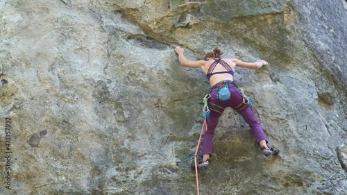 Young woman climber falling down after failed attemp to climb steep wall of rocky mountain. Engaging in extreme sport concept photo