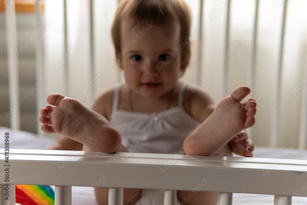 Cute little infant toddler baby girl kid sitting playing Rainbow Pop it finger fidget toy in white crib in white summer pajama with pillow at home. Childhood, leisure, comfort, development concept Cute little infant toddler baby girl kid sitting playing Rainbow Pop it finger fidget toy in white crib in white summer pajama with pillow at home. Childhood, leisure, comfort, development concept