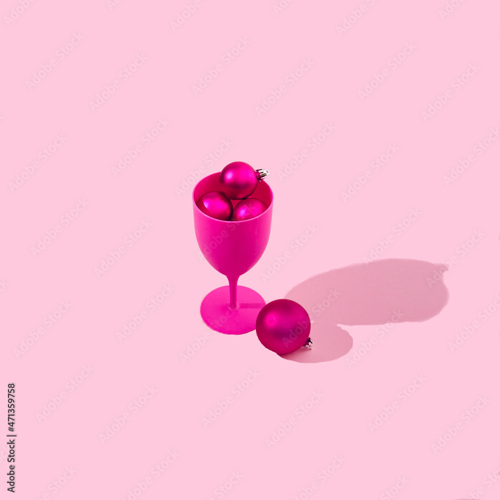Fototapeta premium A fuchsia wine or cocktail glass full of fuchsia Christmas baubles on pastel pink background. Monochrome colors for Christmas or New Year celebration banner or advertisement.
