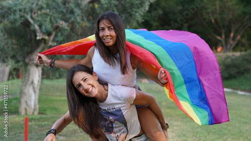 Chicas jóvenes lesbianas con bandera LGTBI jugando llevándose a coscoletas o al caballito photo