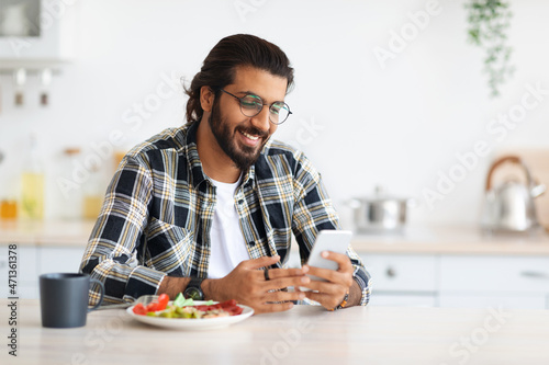 Cheerful middle-eastern guy enjoying lunch  using mobile phone