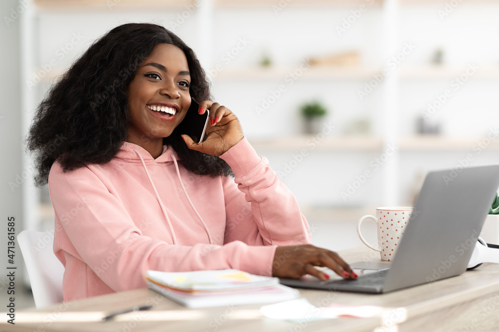 Pretty black lady having phone conversation while working on laptop Pretty black lady having phone conversation while working on laptop