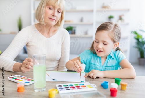 Mature woman and girl drawing with watercolor painting at home
