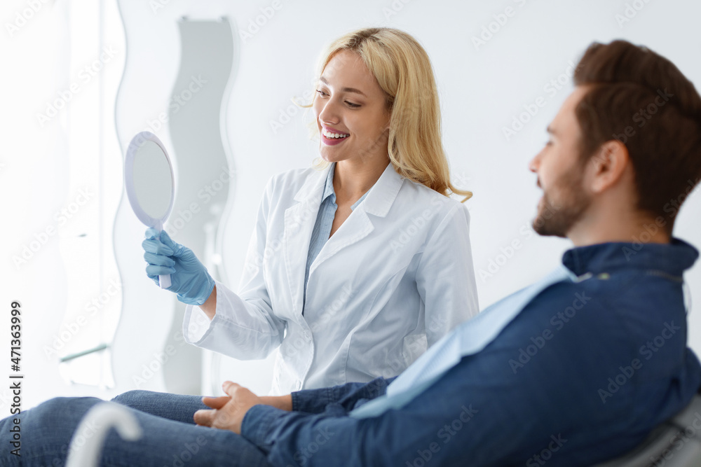 Pretty woman dentist holding mirror for male patient