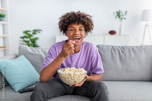 Cheery African American teenager with bowl of popcorn enjoying funny movie, laug Fototapet
