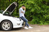 Puzzled arab man standing by open car hood