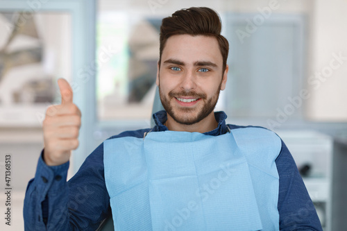 Young man patient smiling in dentistry, showing thumb up
