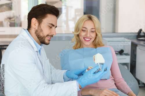 Dentist showing female patient jaw model, dental clinic interior