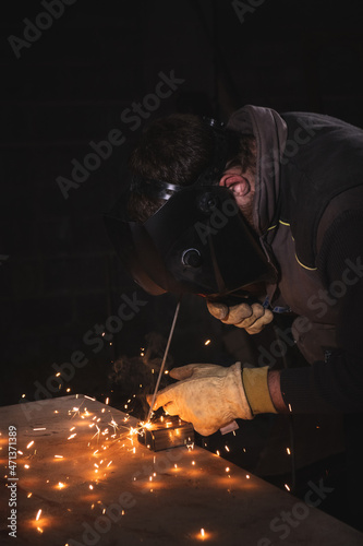 Welder welding a metal plate with yellow sparks in a factory
