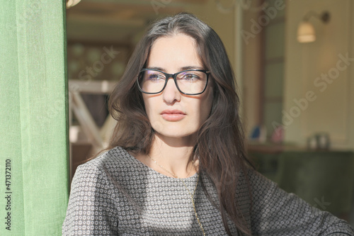 asian mixed race woman sitting in a cafe and looking aside. young beautiful businesswoman wearing glasses thinking alone. calm and thoughtful lady with long brown hair