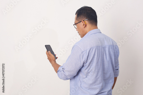 Back view of Adult Asian man wearing bright blue shirt looking to mobile phone screen. Isolated on white