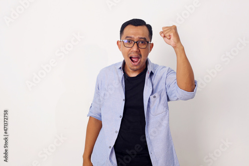 Happy energetic young Asian man yelling and clenching fists isolated on white studio background © SetianingDyah