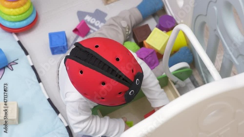 Cute toddler playing with soft montessori building blocks in baby playpen with play mat for babies and toddlers, 8 month old baby boy wearing safety helmet enjoy playing time in kids activity centre. photo