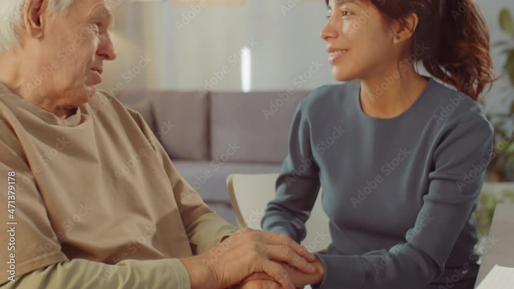 Loving grandfather spending time with his granddaughter sitting close to each other, holding hands and talking about something, handheld tilt up shot