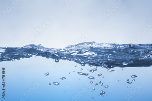 Water splash on blue background. Aqua flowing in waves and creating bubbles. Drops on the water surface feel fresh and clean.