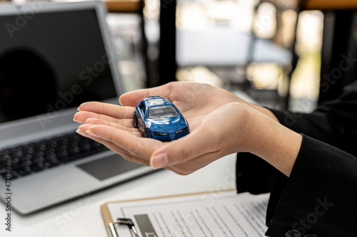 A person using two hands holding a small blue car model, a female employee of a car rental company holding a model car in two hands. Car rental concept. © kamiphotos