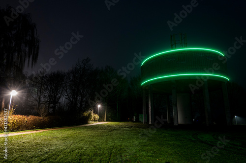 Bronderslev, Denmark,  A water tower highlighted with green lights sits in an illuminated park. photo