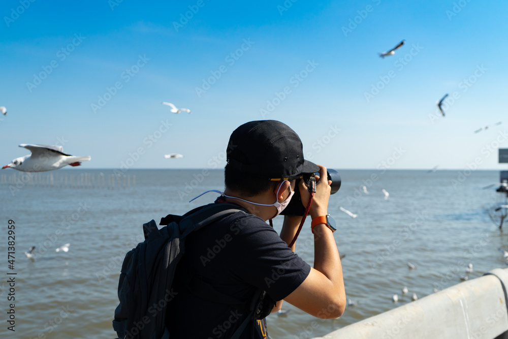 Obraz premium Man photographer or cameraman to wear Hygienic mask or face mask to take a photo of seagull,Bird photography at Bangpoo, Samut Prakan,Thailand.