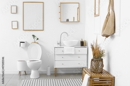 Interior of white restroom with toilet bowl and chest of drawers photo