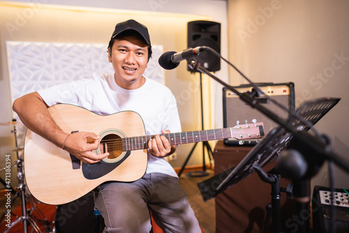 Handsome vocalist smiles for the camera while singing while playing acoustic guitar