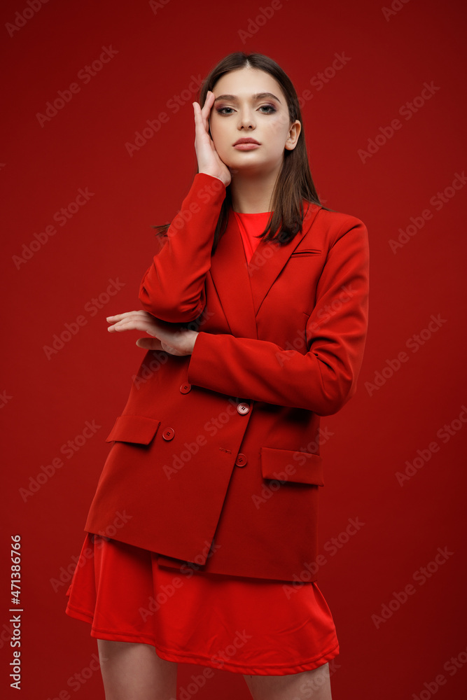 High fashion photo of elegant young model in red suit, jacket, short skirt, socks. Beautiful young woman, slim figure. Studio shot. Red background. Monochrome color High fashion photo of elegant young model in red suit, jacket, short skirt, socks. Beautiful young woman, slim figure. Studio shot. Red background. Monochrome color