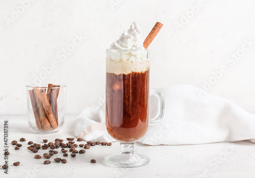 Glass cup of tasty coffee with cinnamon and beans on light background