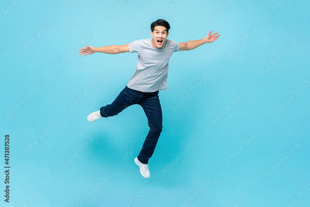 Young Asian man jumping in mid air with hands outstretched on isolated light blue background