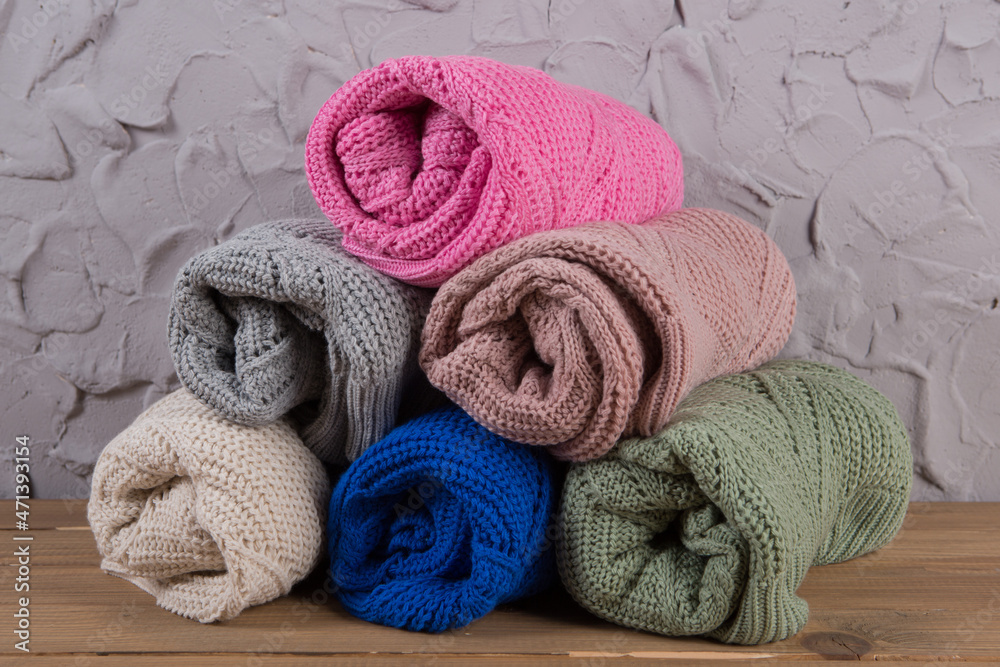 six colored woolen sweaters in rolls on the table, assortment of goods against the background of a concrete loft wall six colored woolen sweaters in rolls on the table, assortment of goods against the background of a concrete loft wall